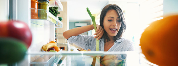 Closeup of a cheerful young couple picking some fruit and veggies from the fridge to make some healthy breakfast on Sunday morning. Shot from inside the working fridge.